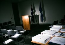 Australia impulsa proyecto fiscal cripto bajo OCDE Podio de madera y sillas vacias en una sala gubernamental iluminada por flash directo (imagen generada por IA)