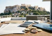 Grecia gravará las ganancias cripto con un 15% Mesa con documentos financieros, monedas y calculadora frente a la vista del Partenón (imagen generada por IA)
