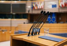Euro digital inminente según el BCE frente a la inflación Atril de madera con micrófonos de prensa en una sala institucional europea con luz natural (imagen generada por IA)