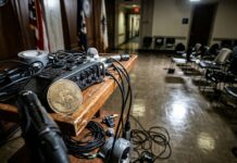 Bitcoin bajo presión por inflación: CoinShares matiza Ficha metálica de criptomoneda sobre un atril con cables en una sala de prensa vacía (imagen generada por IA)